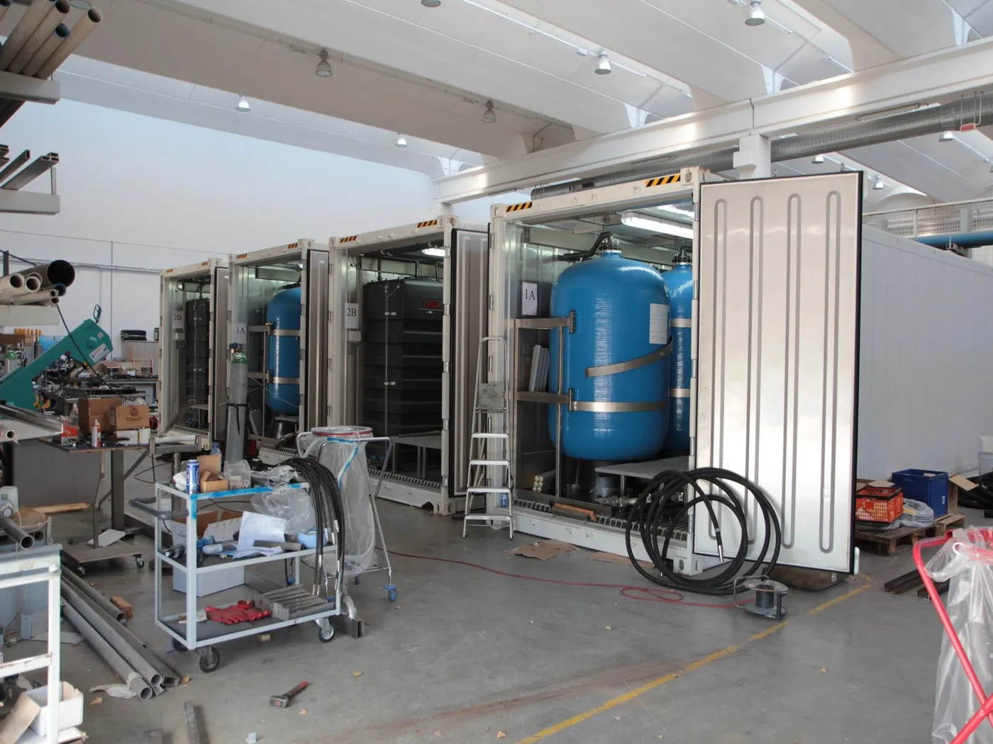 Open containers with blue pressure vessels being fitted out in a workshop hall