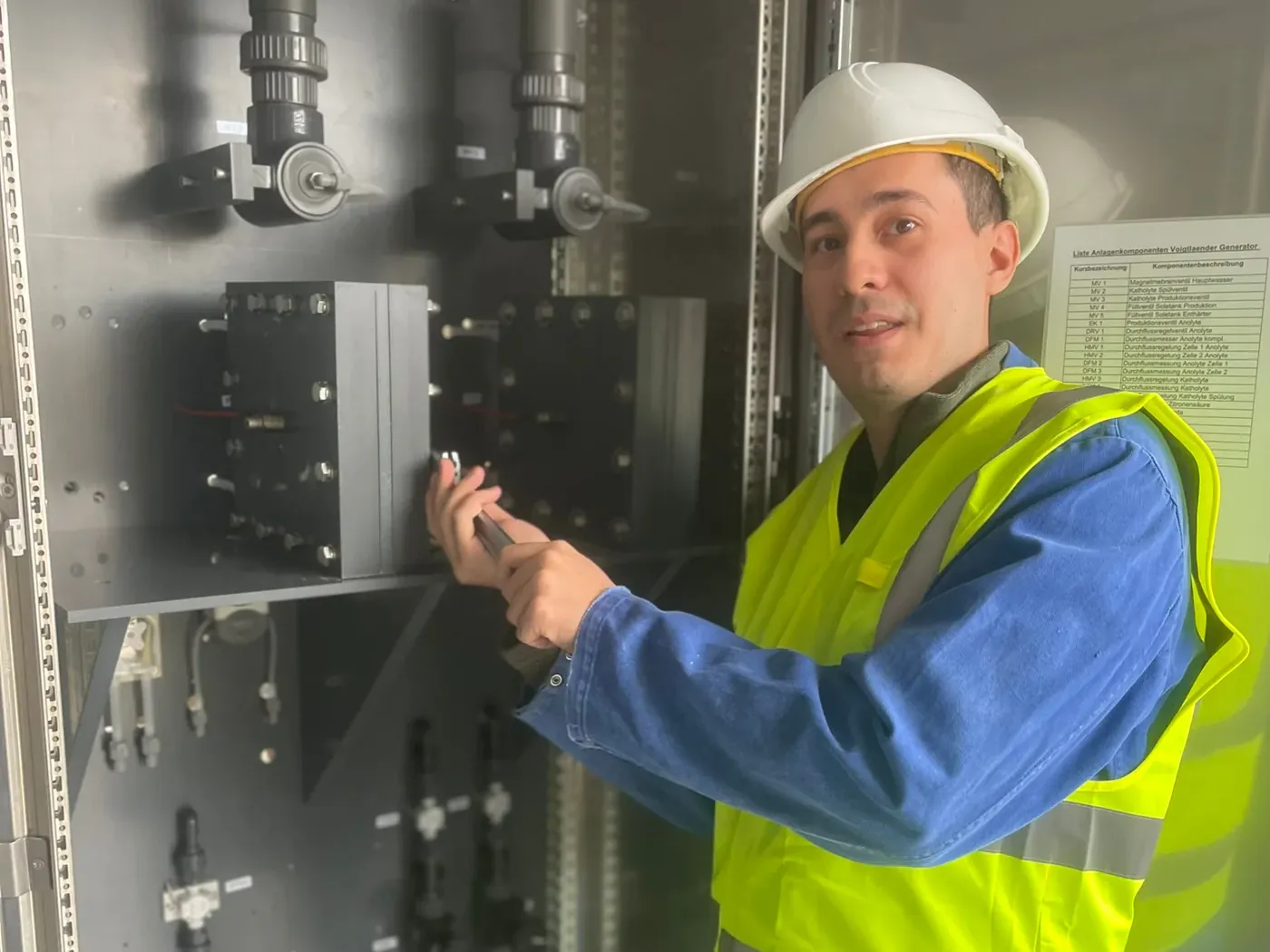 Technician in hard hat and high-visibility vest working at an open generator cabinet